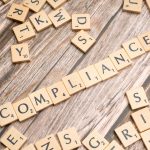 Peças de madeira formam a palavra “COMPLIANCE” sobre uma superfície rústica.