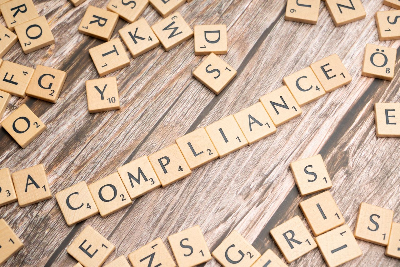Peças de madeira formam a palavra “COMPLIANCE” sobre uma superfície rústica.