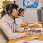 Agentes de atendimento trabalham em computadores usando headsets em um escritório moderno.