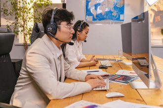 Agentes de atendimento trabalham em computadores usando headsets em um escritório moderno.