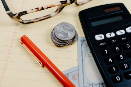 Calculadora, moedas e óculos sobre um bloco de anotações em uma mesa de trabalho financeiro